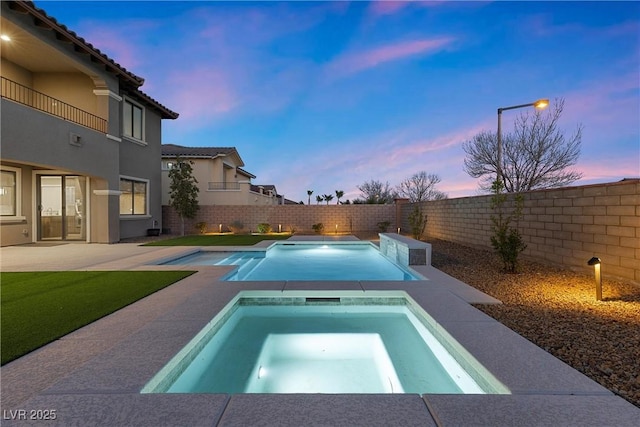 pool at dusk featuring an in ground hot tub, a patio area, a fenced backyard, and a fenced in pool