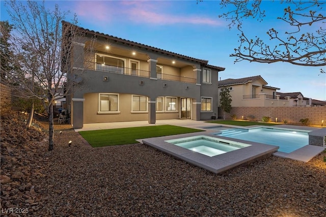 back of property with a balcony, a patio area, an in ground hot tub, and stucco siding