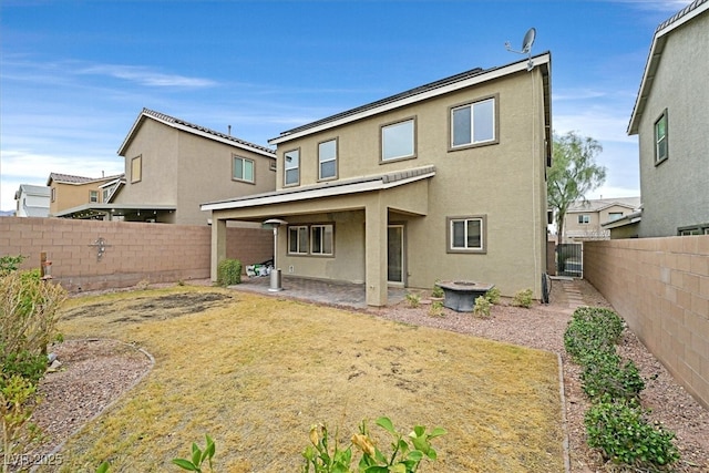 rear view of house featuring stucco siding, a fenced backyard, a fire pit, and a patio