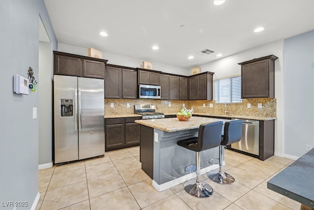 kitchen featuring dark brown cabinetry, decorative backsplash, a center island, stainless steel appliances, and light tile patterned flooring