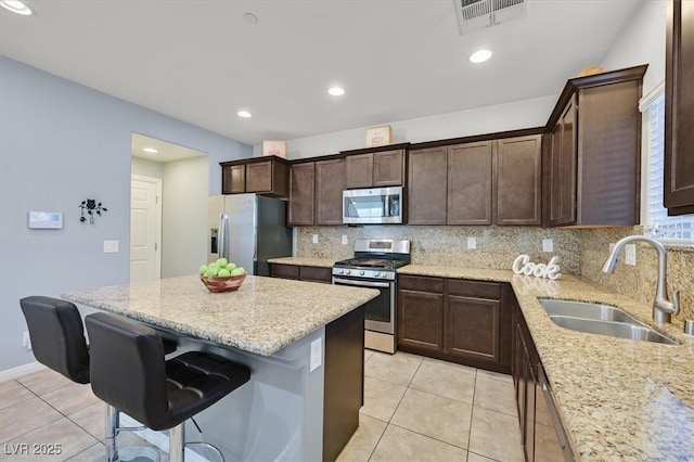 kitchen featuring stainless steel appliances, a breakfast bar, a sink, visible vents, and backsplash