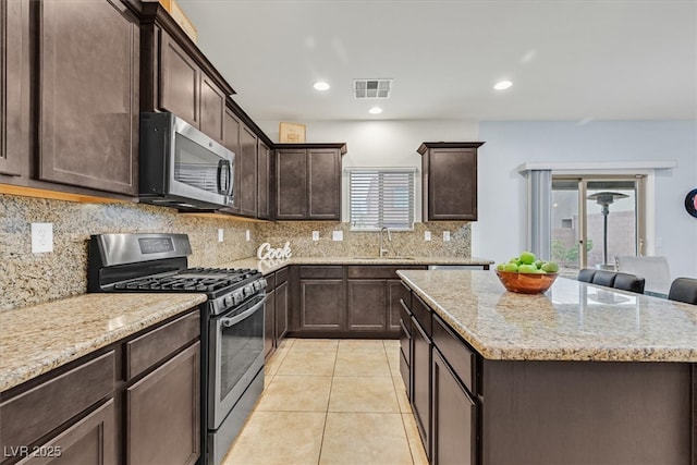 kitchen with light tile patterned floors, visible vents, a kitchen island, appliances with stainless steel finishes, and dark brown cabinets