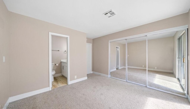 unfurnished bedroom with a closet, connected bathroom, and light colored carpet