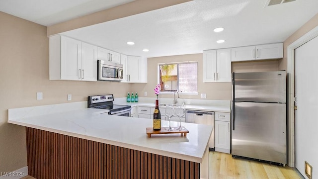 kitchen with a sink, white cabinetry, appliances with stainless steel finishes, a peninsula, and light countertops