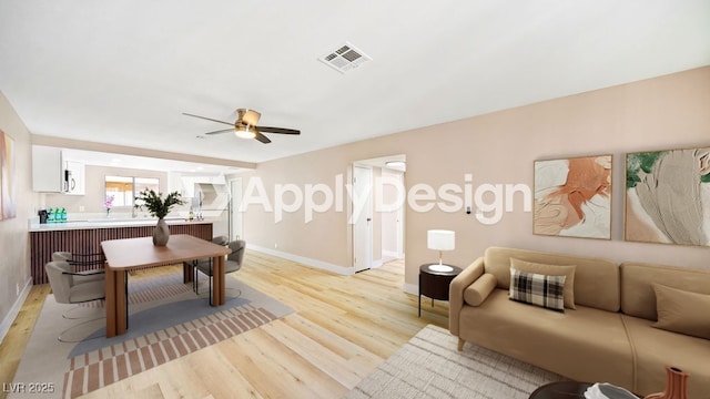 living area with light wood-style flooring, baseboards, visible vents, and ceiling fan