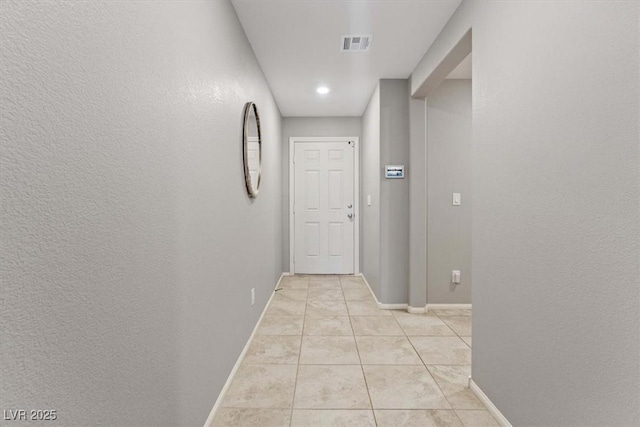 hallway with light tile patterned floors, baseboards, visible vents, and a textured wall