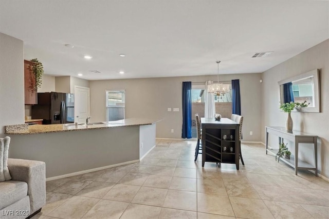 kitchen with black fridge with ice dispenser, an inviting chandelier, light stone counters, light tile patterned floors, and pendant lighting