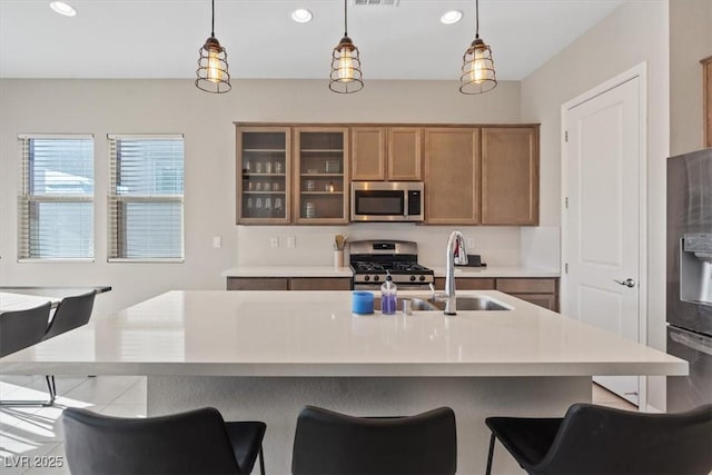 kitchen with an island with sink, appliances with stainless steel finishes, sink, and pendant lighting