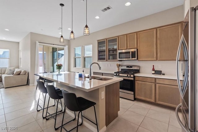 kitchen with a center island with sink, hanging light fixtures, sink, light tile patterned floors, and appliances with stainless steel finishes