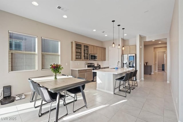 kitchen with appliances with stainless steel finishes, pendant lighting, light tile patterned floors, sink, and a kitchen island with sink