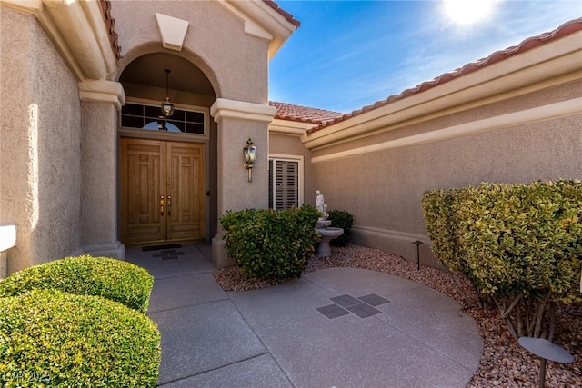 view of exterior entry with a tiled roof and stucco siding