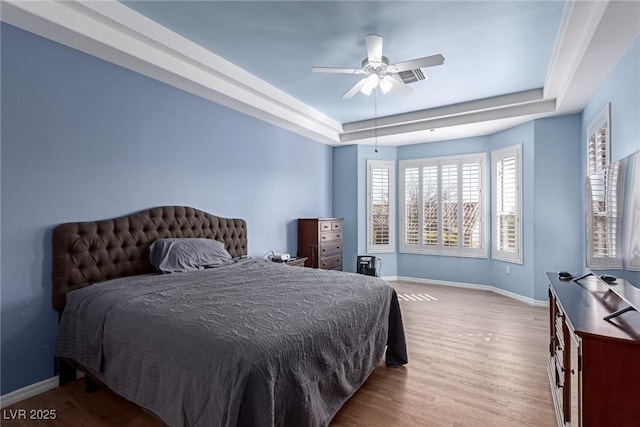 bedroom with light wood-style floors, a tray ceiling, ceiling fan, and baseboards