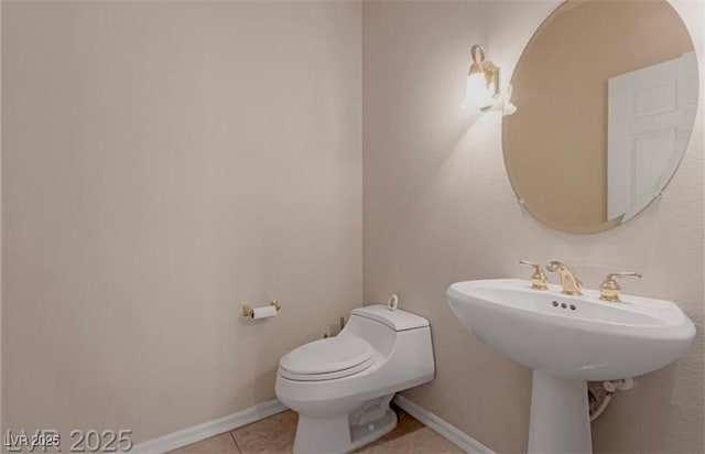 half bath with toilet, tile patterned flooring, baseboards, and a sink