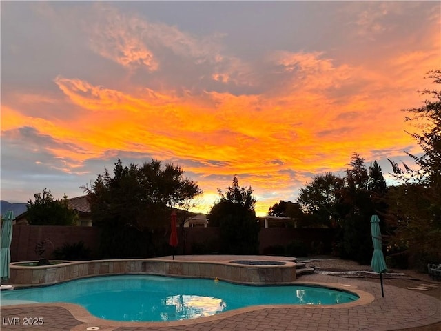 pool at dusk featuring an in ground hot tub, a patio area, a fenced backyard, and a fenced in pool