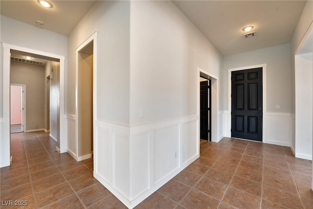 corridor featuring wainscoting, visible vents, and a decorative wall