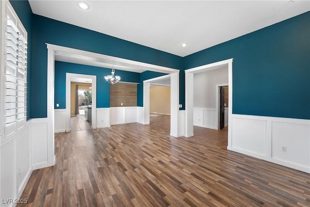 spare room with a chandelier, dark wood finished floors, and wainscoting