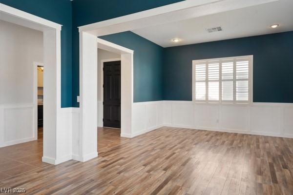 unfurnished room featuring wainscoting, visible vents, and wood finished floors