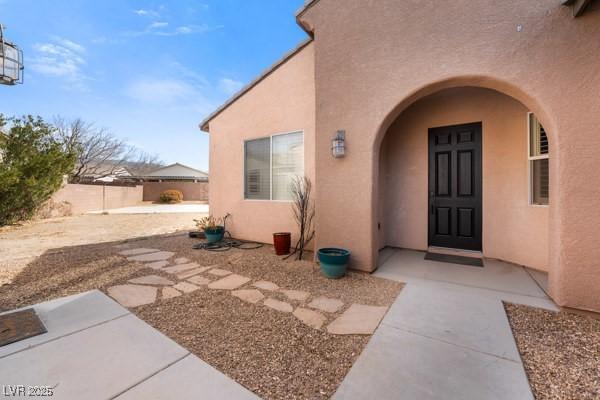 view of exterior entry with fence and stucco siding