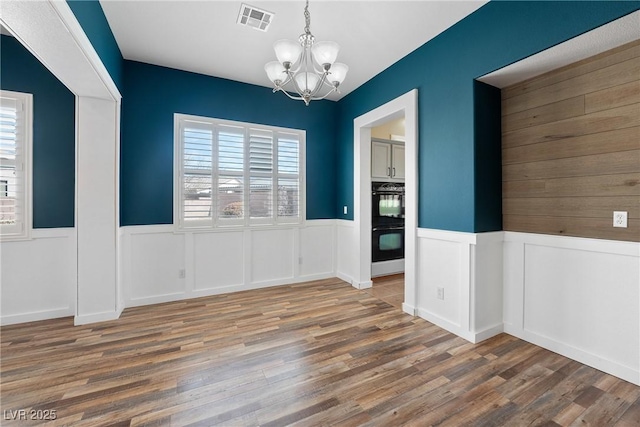 unfurnished dining area with plenty of natural light, visible vents, a notable chandelier, and wood finished floors