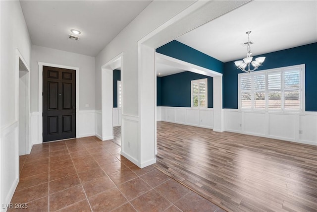 entrance foyer featuring an inviting chandelier, visible vents, dark wood-style flooring, and a wainscoted wall