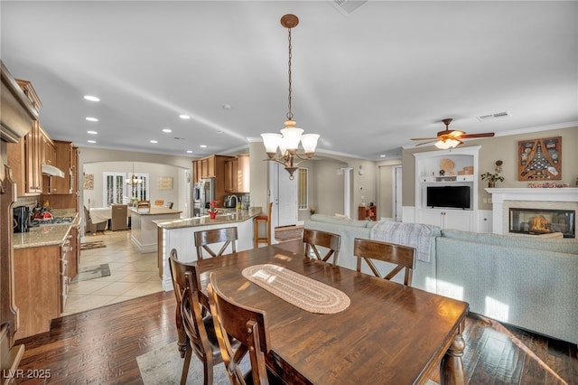 dining room with ceiling fan with notable chandelier, a glass covered fireplace, visible vents, and crown molding