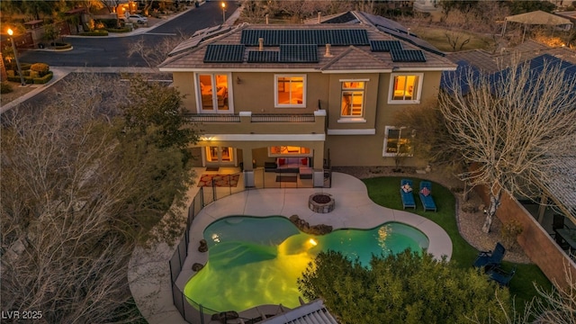 back of house with a patio area, stucco siding, solar panels, and an outdoor living space with a fire pit