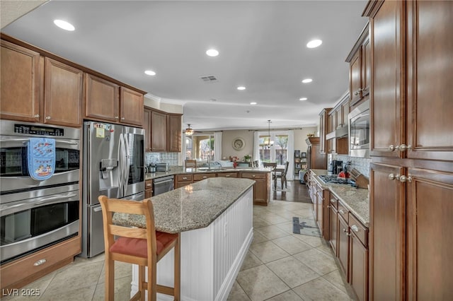 kitchen with a kitchen breakfast bar, a peninsula, light stone countertops, stainless steel appliances, and pendant lighting