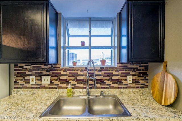 kitchen featuring light stone counters, backsplash, a sink, and dark cabinets