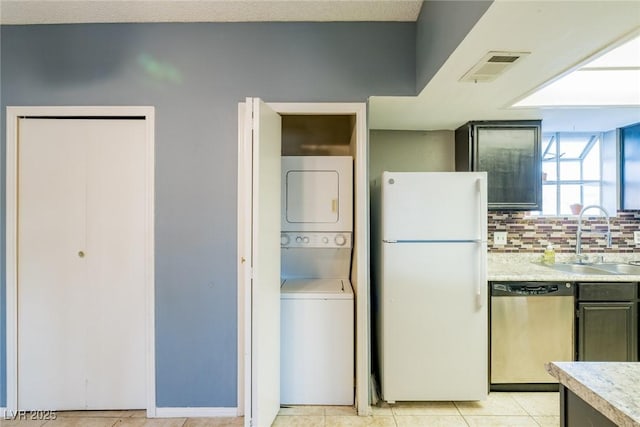 kitchen with a sink, light countertops, stacked washing maching and dryer, freestanding refrigerator, and dishwasher