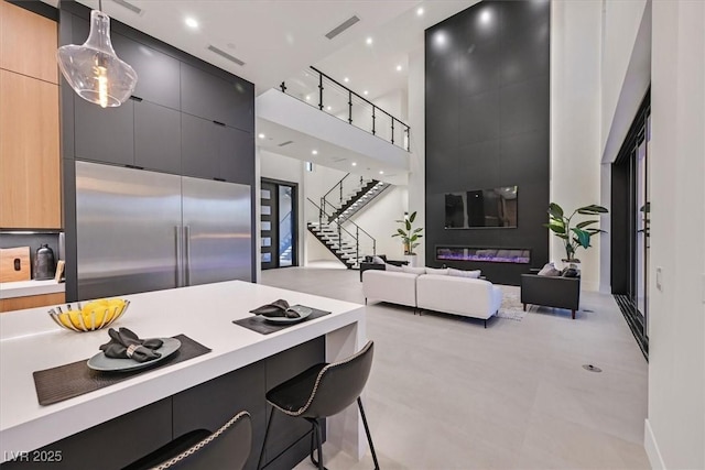 kitchen with a towering ceiling, decorative light fixtures, stainless steel built in refrigerator, a kitchen bar, and light brown cabinetry