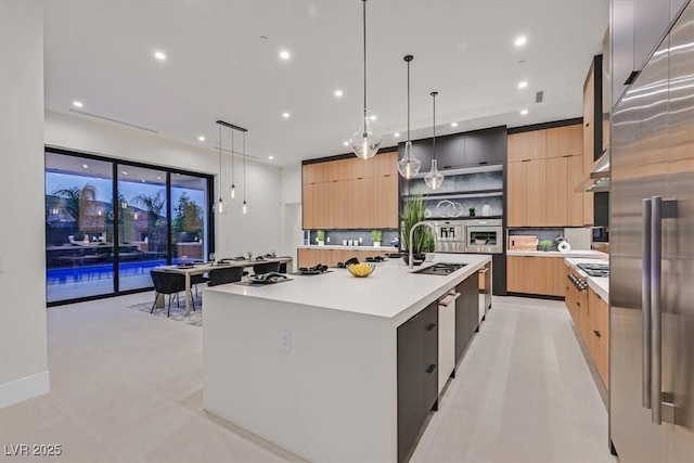 kitchen featuring light brown cabinetry, decorative light fixtures, high quality fridge, a spacious island, and sink
