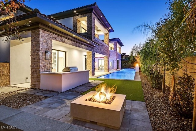 back house at dusk featuring an outdoor fire pit, a patio, area for grilling, and a bar