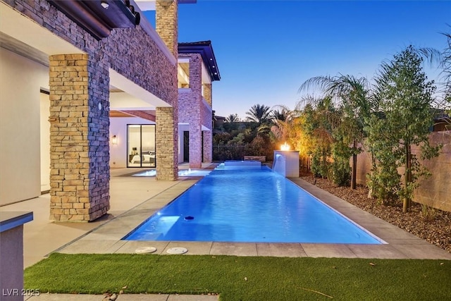 pool at dusk featuring pool water feature and a patio area