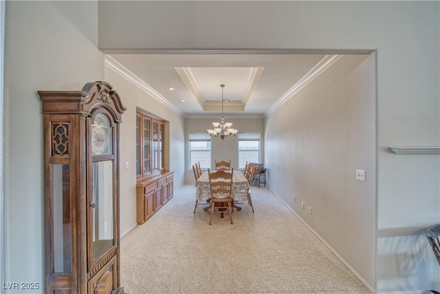 carpeted dining room with ornamental molding, a raised ceiling, and an inviting chandelier