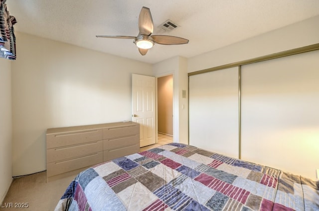 bedroom featuring ceiling fan, light carpet, a textured ceiling, and a closet