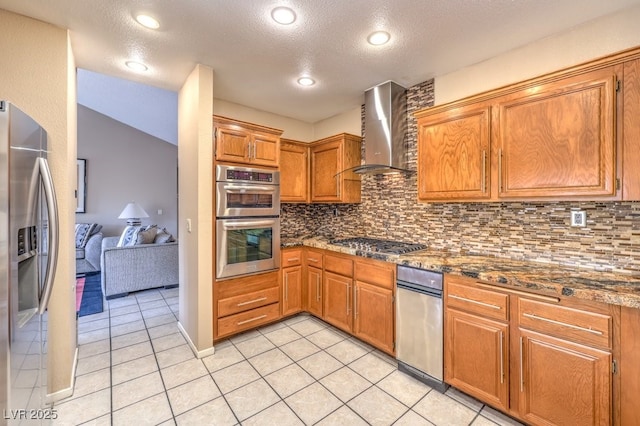 kitchen with appliances with stainless steel finishes, tasteful backsplash, light tile patterned floors, dark stone countertops, and wall chimney range hood