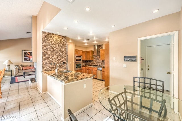 kitchen with kitchen peninsula, sink, stone counters, wall chimney range hood, and double oven