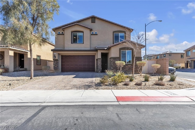 traditional-style house with decorative driveway, stucco siding, fence, a garage, and stone siding