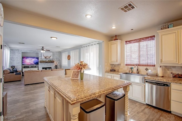 kitchen with a large fireplace, a kitchen island, dishwasher, cream cabinetry, and sink