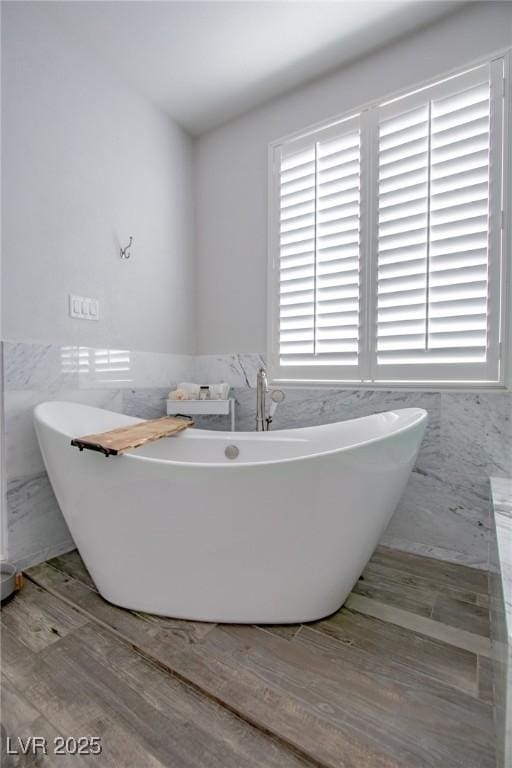 bathroom with a washtub, wood-type flooring, and tile walls