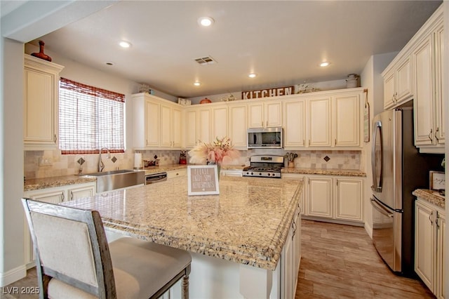 kitchen with a center island, a kitchen breakfast bar, light stone counters, appliances with stainless steel finishes, and sink