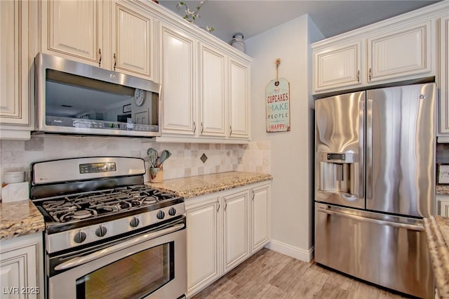 kitchen with light stone counters, decorative backsplash, stainless steel appliances, and light hardwood / wood-style flooring