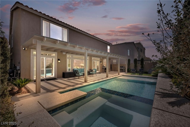 back of property at dusk featuring stucco siding, a pool with connected hot tub, a tiled roof, and a patio area