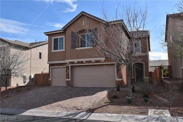 view of front of property featuring fence, stone siding, decorative driveway, stucco siding, and an attached garage