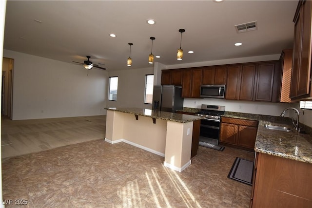 kitchen featuring a sink, dark stone countertops, appliances with stainless steel finishes, and hanging light fixtures