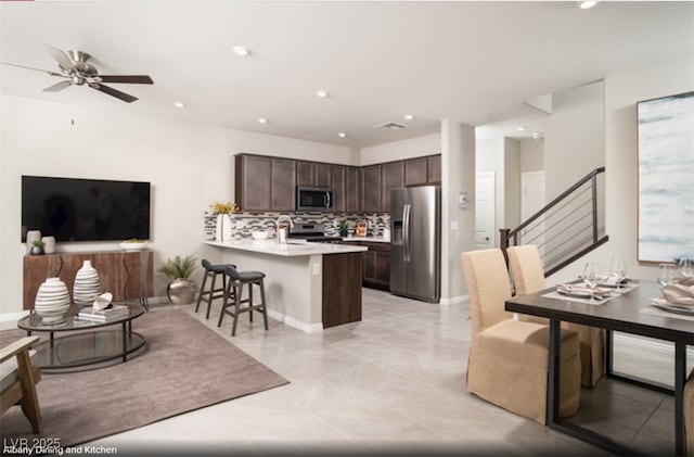 kitchen featuring appliances with stainless steel finishes, open floor plan, a kitchen breakfast bar, a peninsula, and light countertops