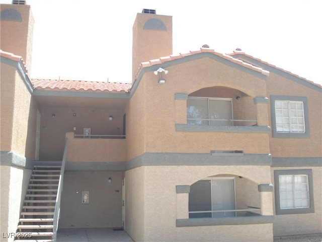 exterior space with stairs, a chimney, a tiled roof, and stucco siding