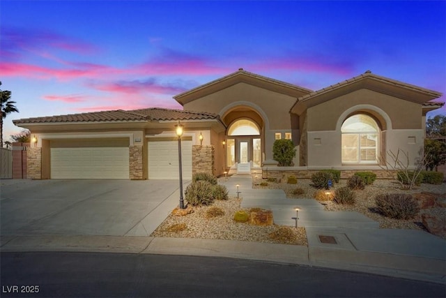 mediterranean / spanish home with concrete driveway, stone siding, a tile roof, an attached garage, and stucco siding