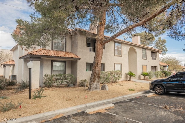 view of front of house with uncovered parking, central air condition unit, a tiled roof, and stucco siding