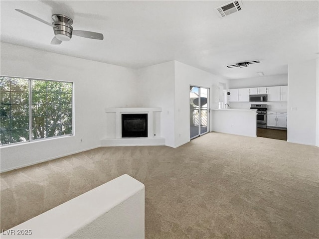 carpeted living room with visible vents, a fireplace with raised hearth, and a ceiling fan